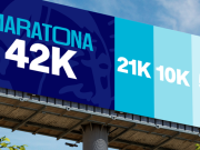 Outdoor publicitário da Maratona de Tubarão 2026 exibindo as distâncias de 42K, 21K, 10K e 5K em diferentes tons de azul. No canto direito, o logotipo do evento com a data 24 de maio de 2026 sobre um fundo de céu azul e árvores.